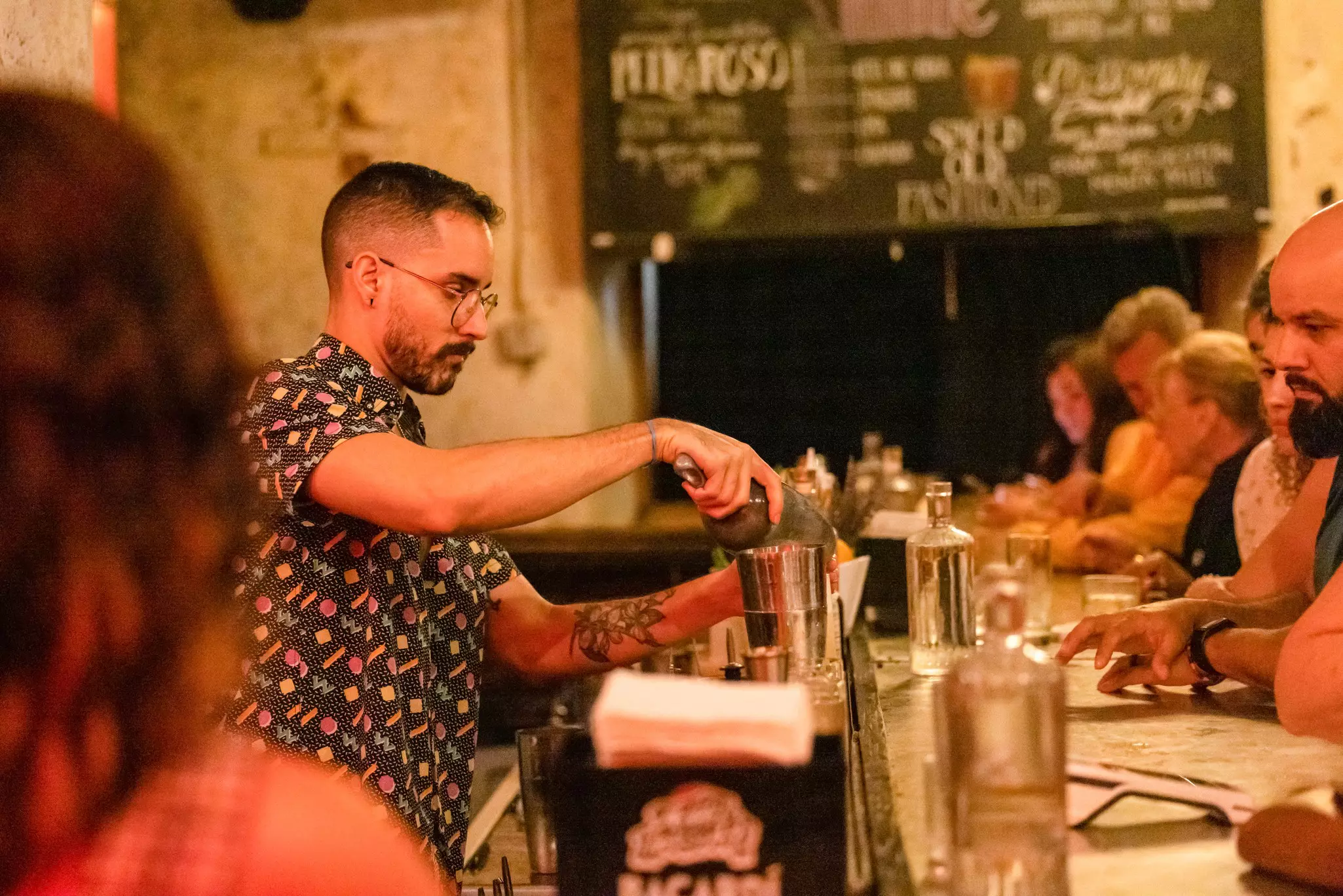 A bartender makes cocktails in a busy bar lined with customers.