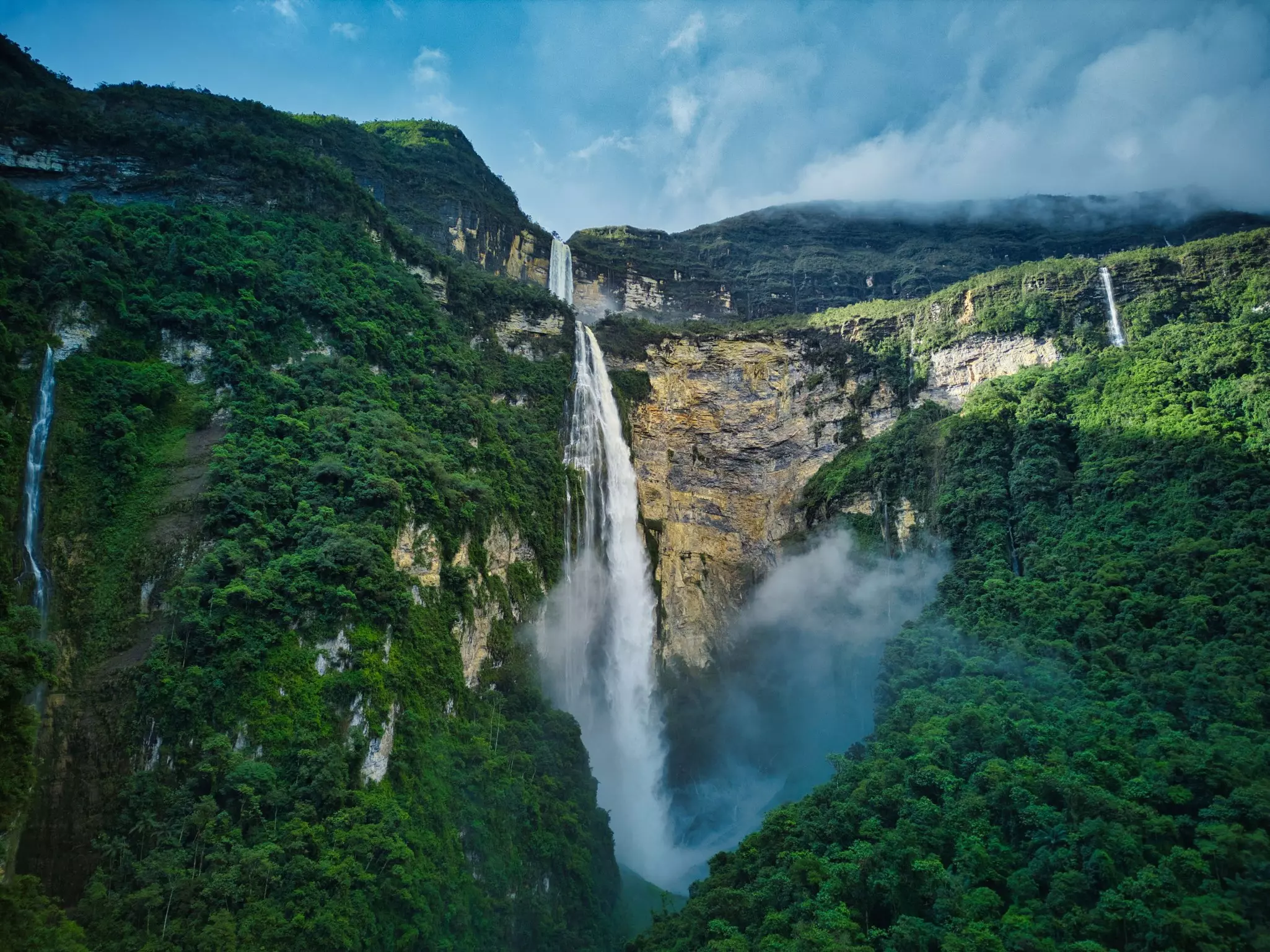 A tiered waterfall cascades down a green mountain with white spray.