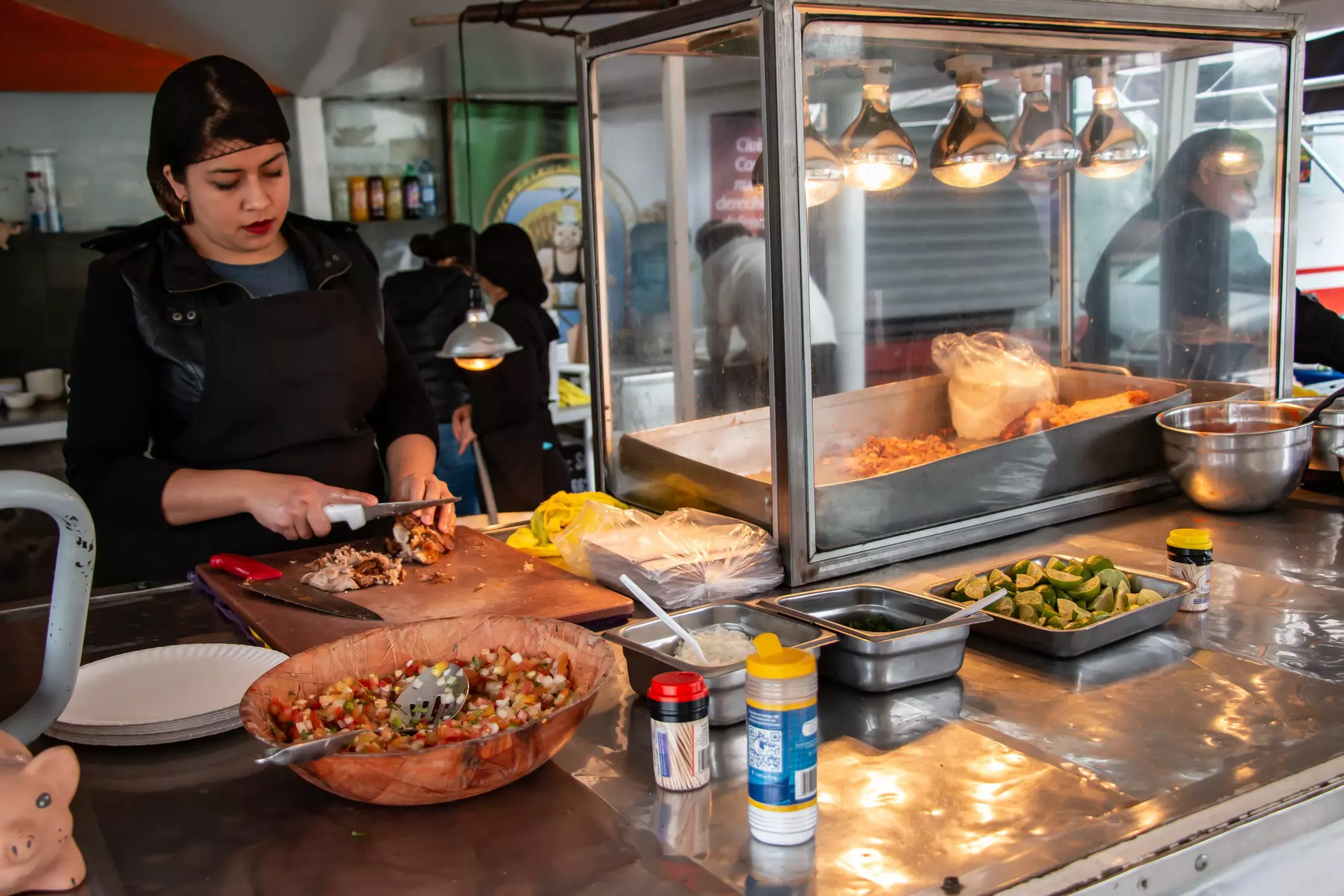 A woman slices meat at a street food stand in a city.