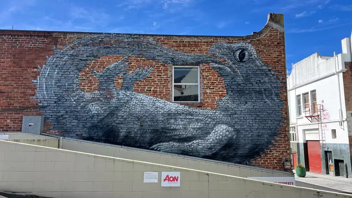 A large mural on a wall of a lizard lying on its back and trying to chew its own tail.