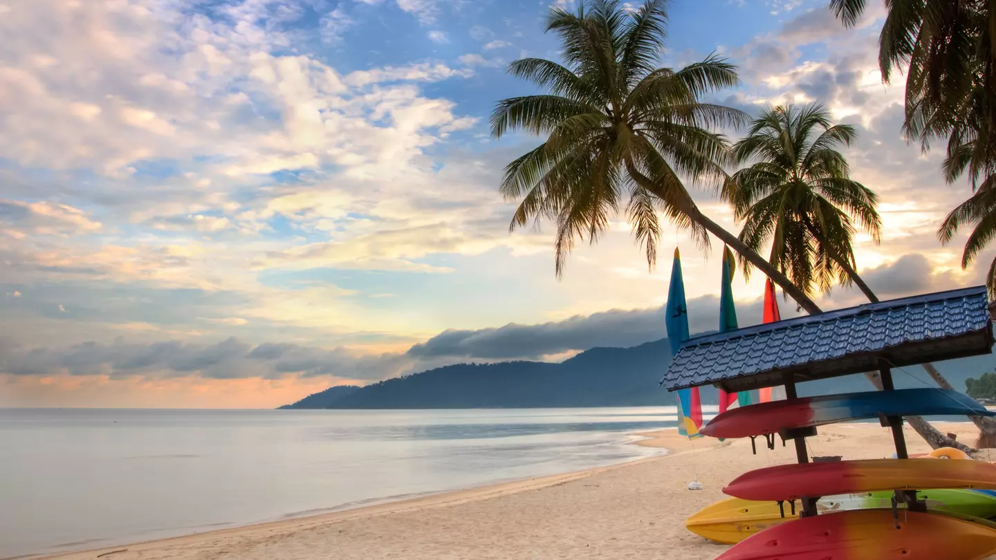 A deserted beach with palms and stored boats on Tioman Island, as the sunrise creates pink and light-blue light