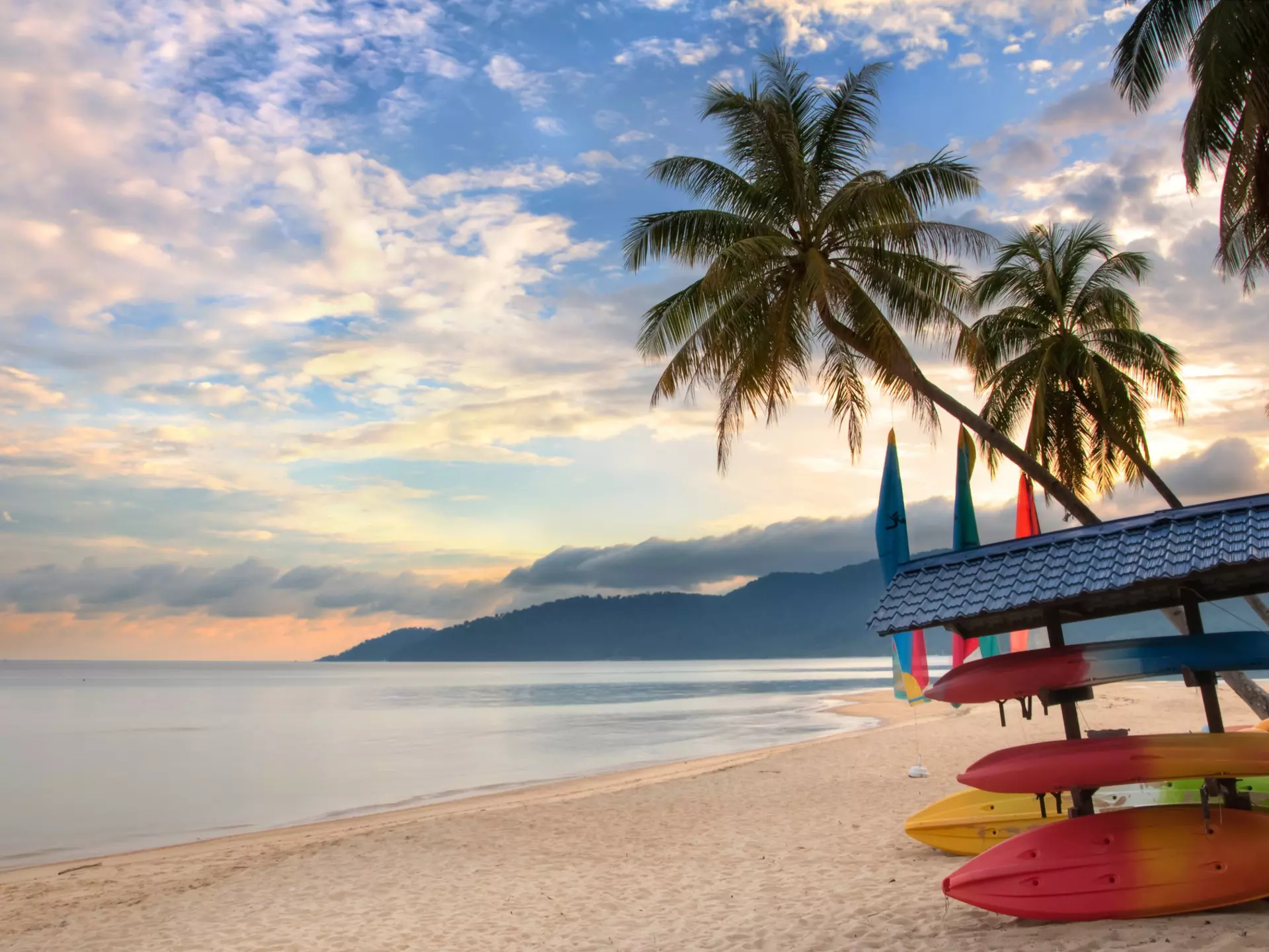A deserted beach with palms and stored boats on Tioman Island, as the sunrise creates pink and light-blue light