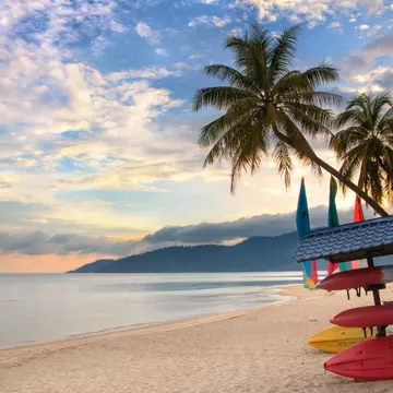 A deserted beach with palms and stored boats on Tioman Island, as the sunrise creates pink and light-blue light