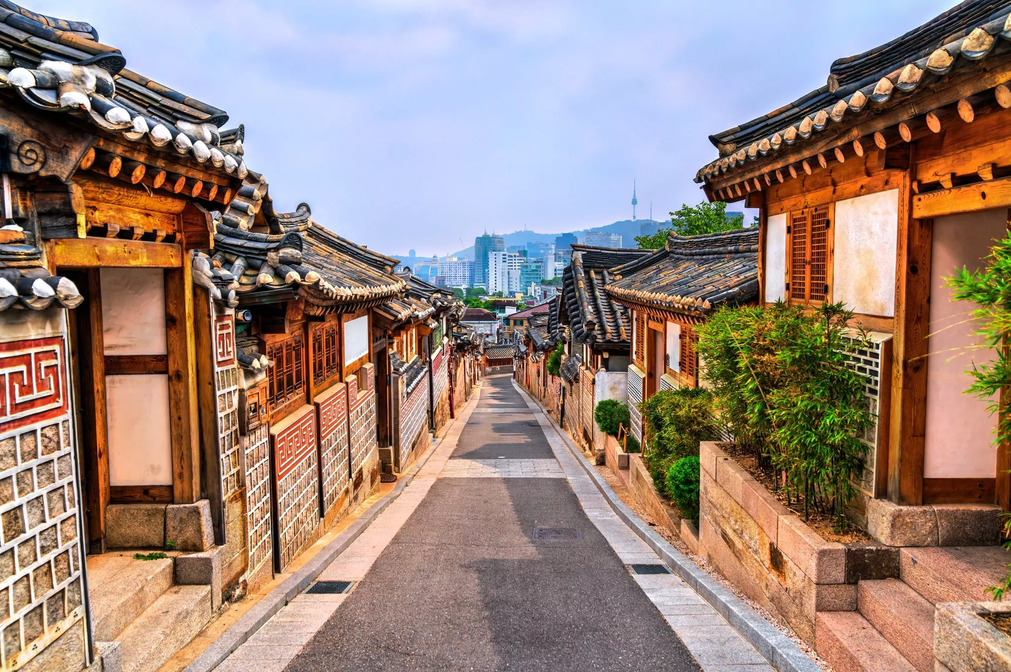 A narrow street slopes downhill, lined with low-rise traditional Korean-style houses