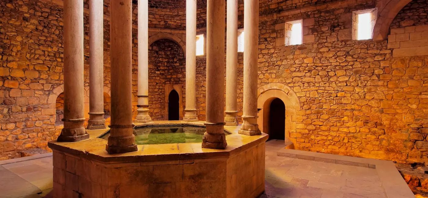 An ancient bathtub framed by stone pillars is located in a historic stone building.