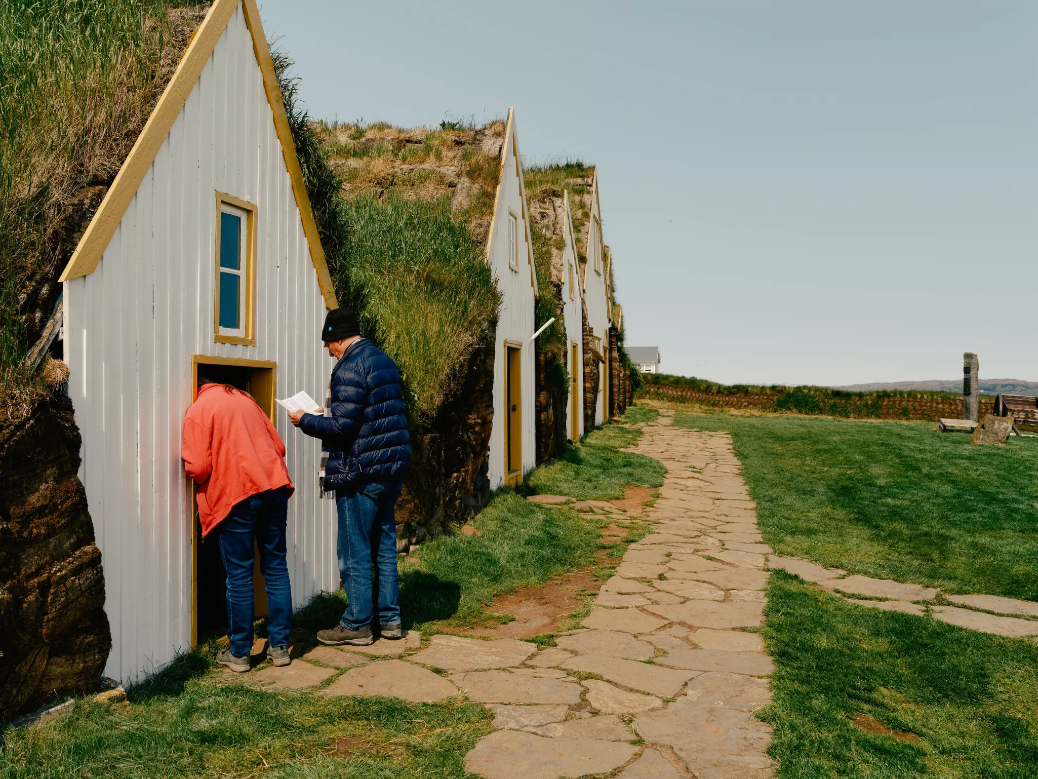 People poke into the doorway of a traditional turf farm cottage, with an earth roof.