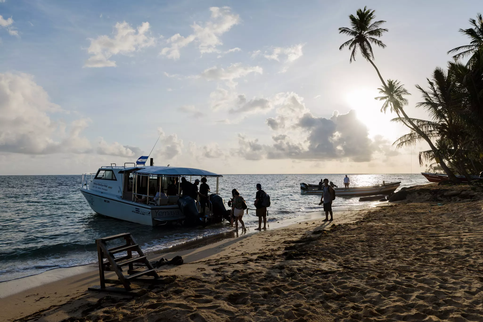 People boarding a small boat directly from a sandy palm tree-lined beach.