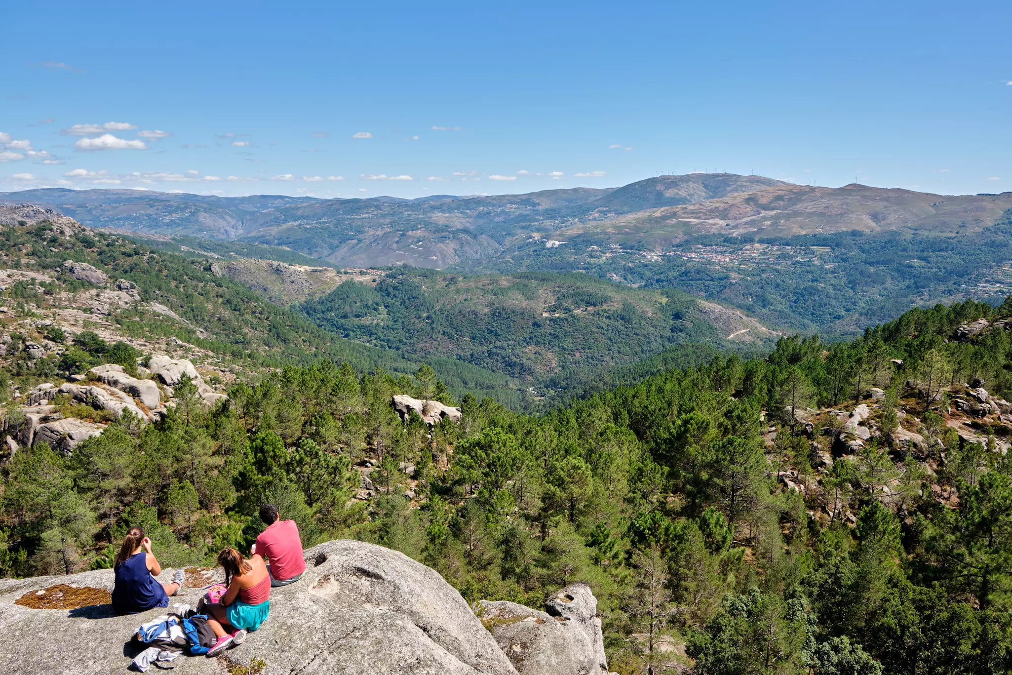 People sitting on rock overlooking forested mountains.