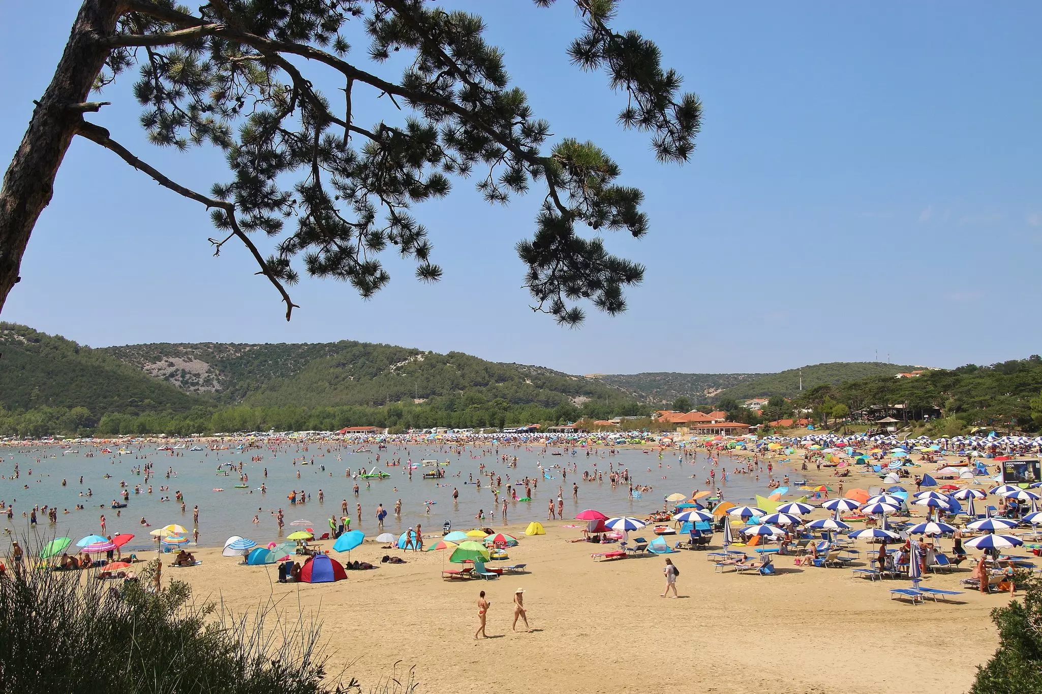 People sunbathing and paddling in the sea at Paradise beach on Rab Island. 