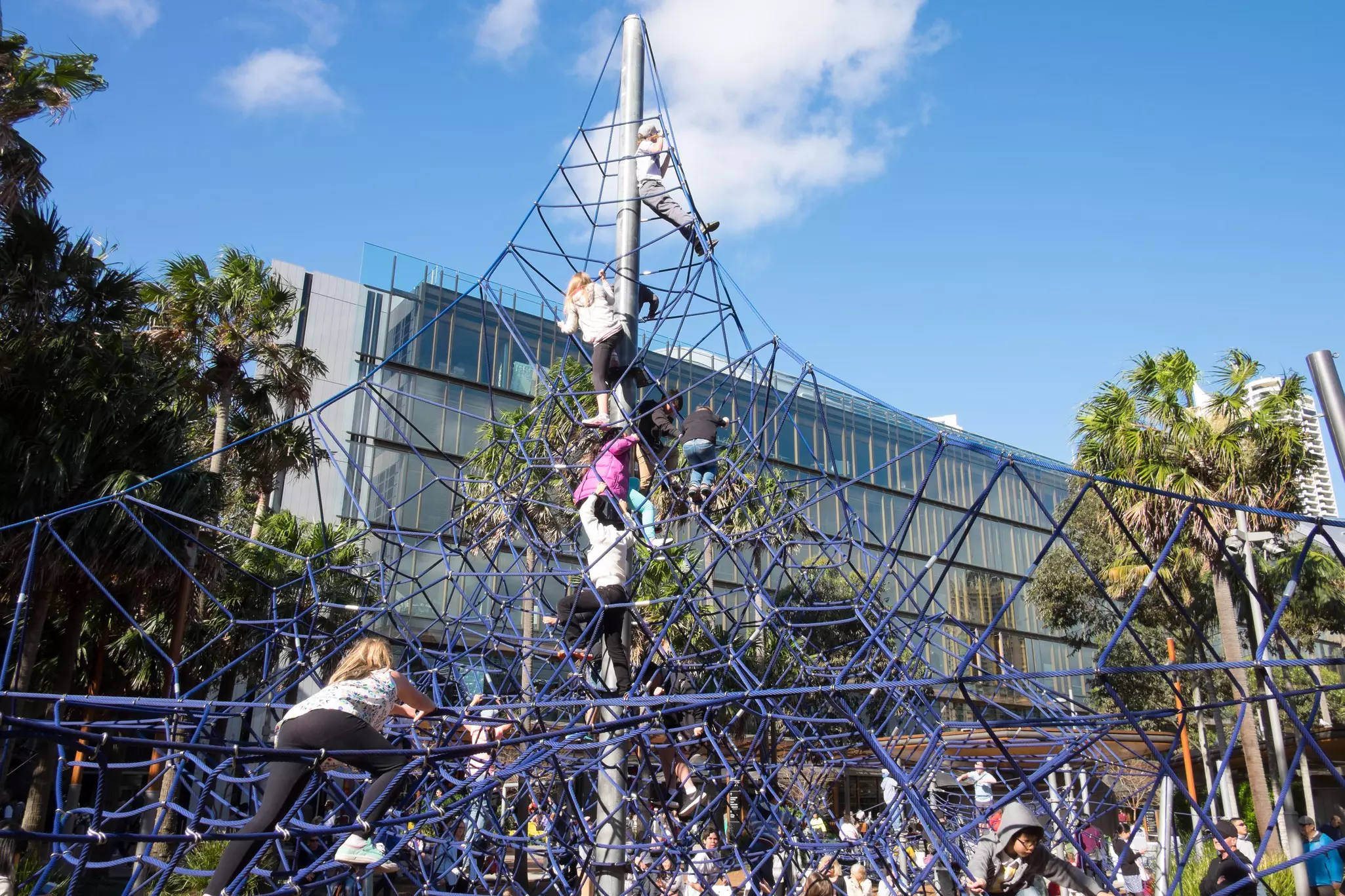 Children play on a rope jungle gym at a playground in a city.