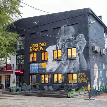 A dark building with a large black-and-white mural of a man with a camera, and outdoor cafe seating.