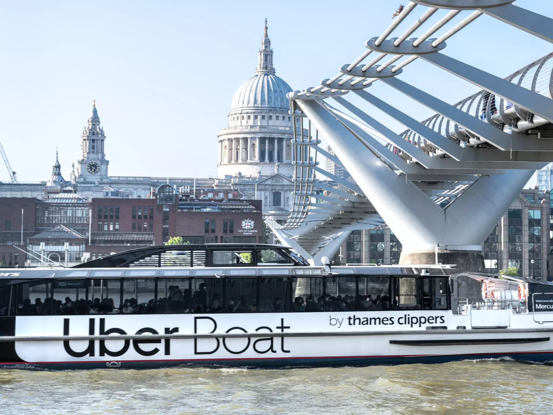 View of an Uber Thames Clipper River Boat passing under the Millennium Footbridge on the River Thames in London, UK.