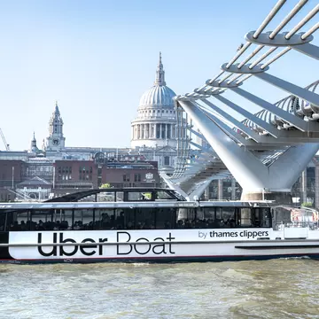 View of an Uber Thames Clipper River Boat passing under the Millennium Footbridge on the River Thames in London, UK.