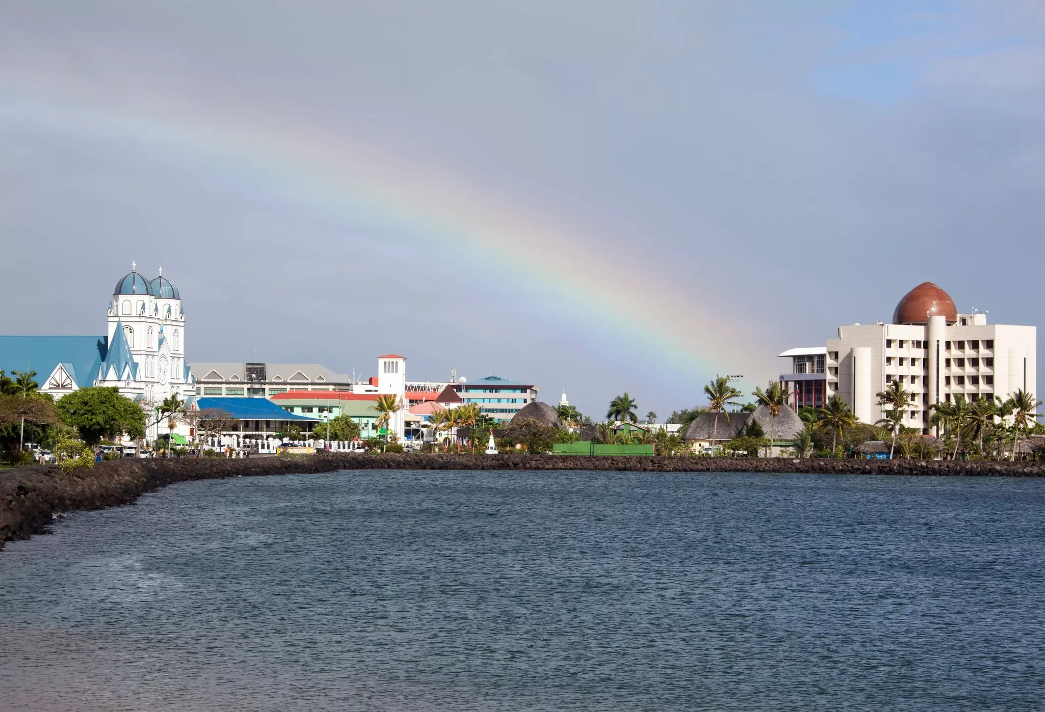 A rainbow above a small coastal city with a large white church building.