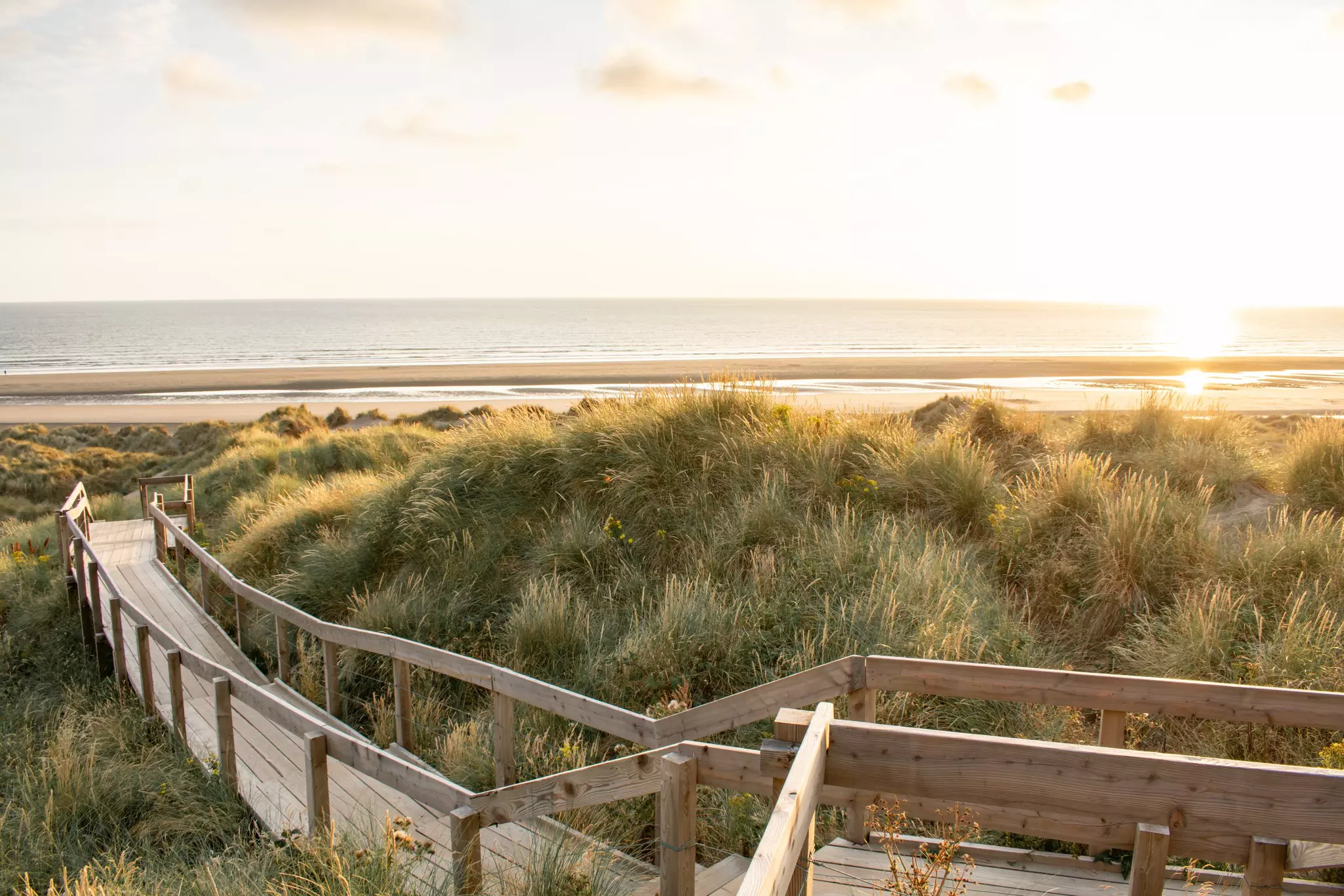 Sand dunes covered in grass and protected from trampers by a wooden boardwalk leading to the beach