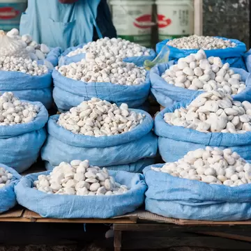 Rows of blue sacks filled with small white dried potatoes on a wooden market stall.