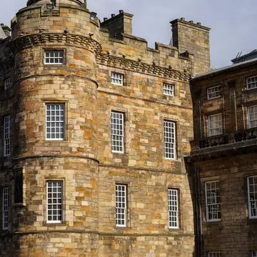 Holyroodhouse Palace Tower stands bathed in sunlight with dramatic shadows, highlighting its historic stone architecture and distinctive conical roof details.
