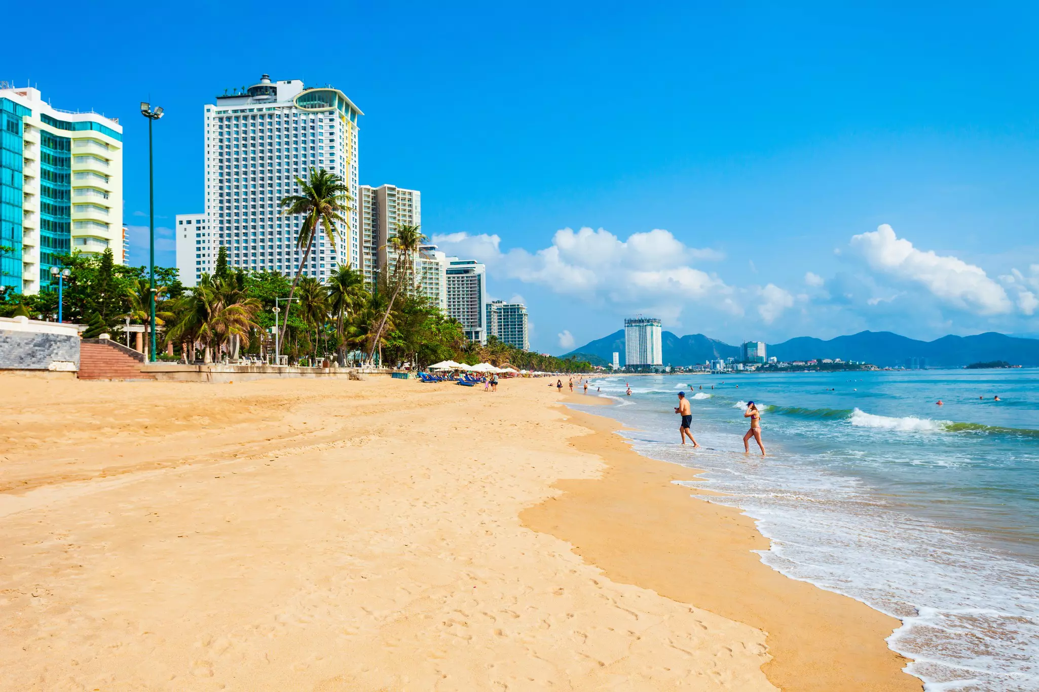 People walk out of the ocean on a quiet city beach backed by high-rise buildings.