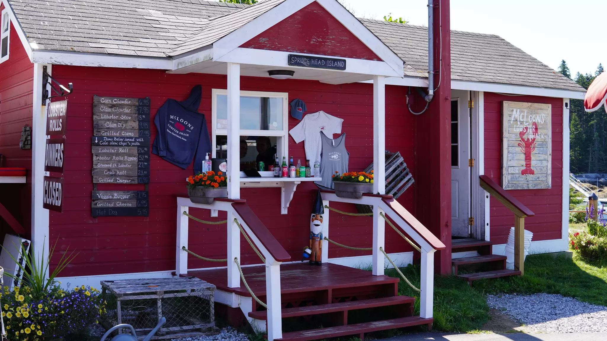 Small red building trimmed in white, with painted boards for signs, sweatshirts and T-shirts pinned to the sides, and a narrow staircase to a window