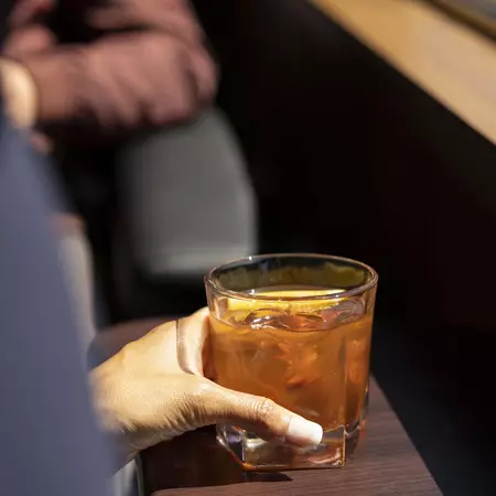 A person's hand holds a small glass with a drink on a train.