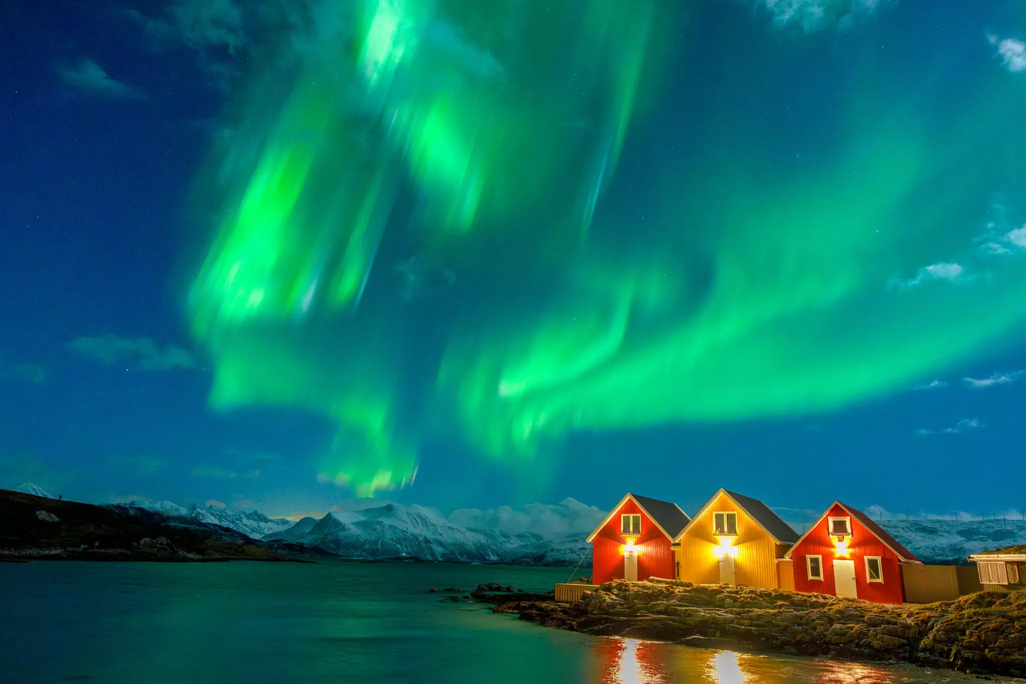 Green northern lights in a dark sky over brightly painted buildings.