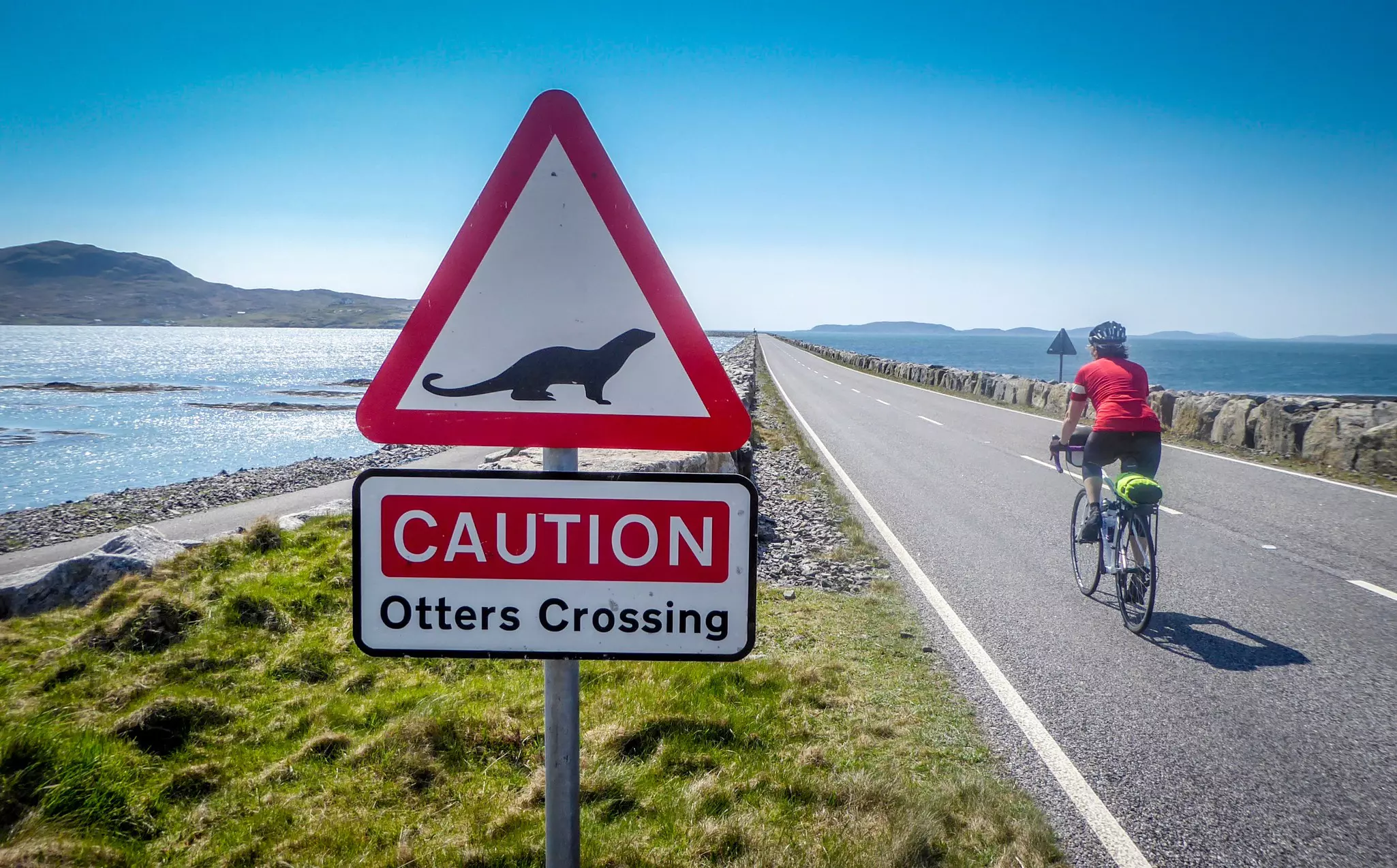 Cyclist passes an Otter Crossing sign in Berneray, Scotland.