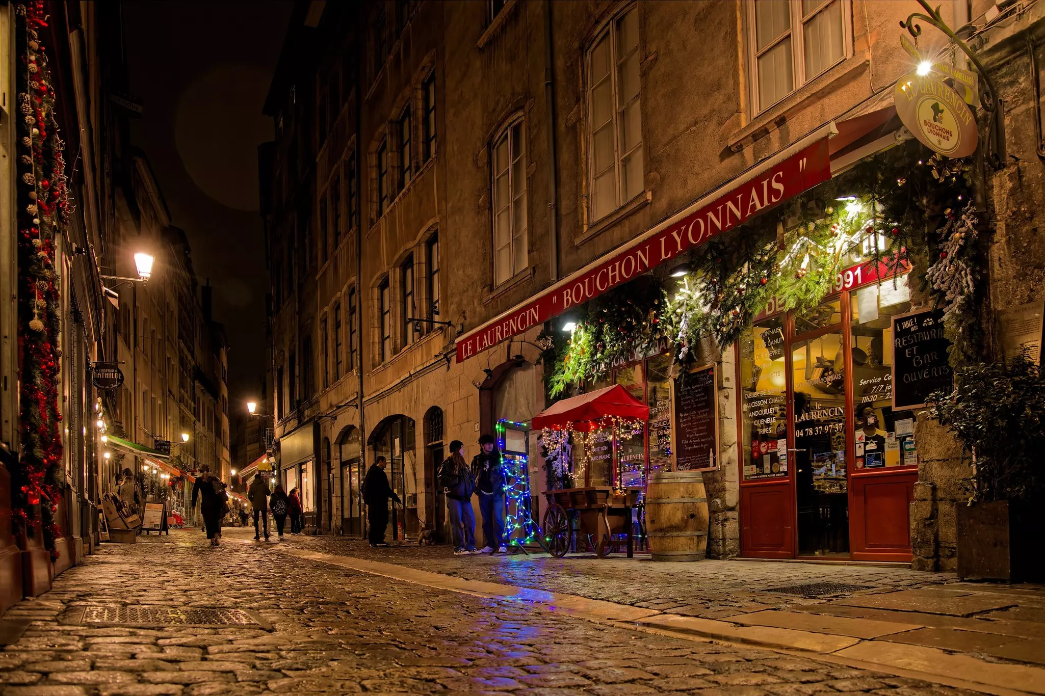 A cobbled street lined with restaurants is lit up at night