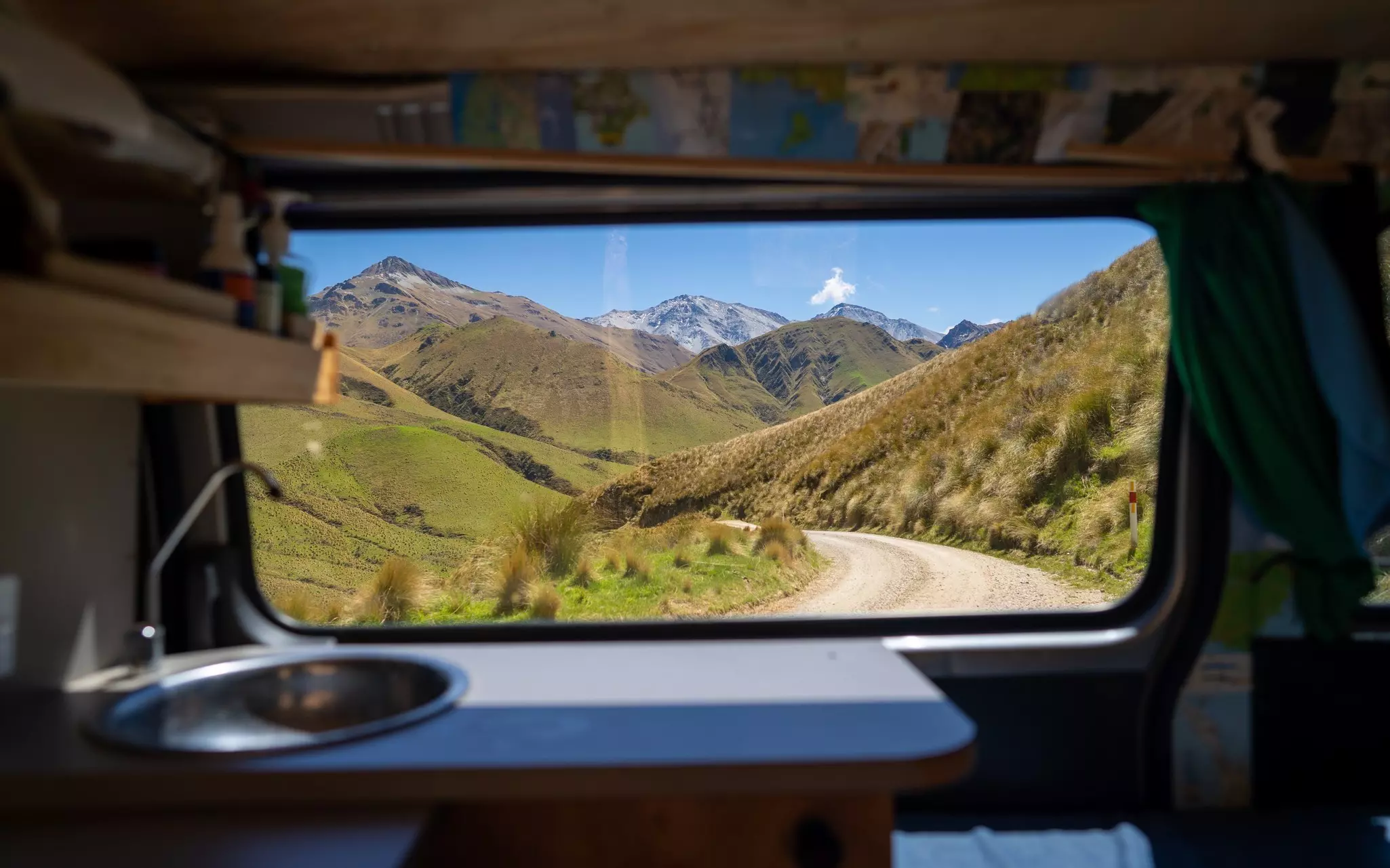 A road is visible through a van window; there is a sink in the foreground, and mountains in the background through the window.