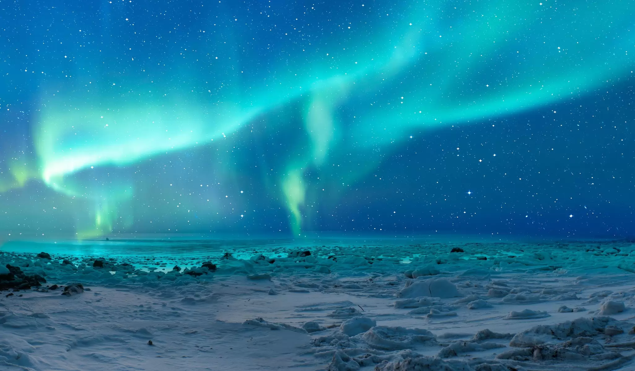 Turquoise, shimmering lights fill the sky above snow-covered terrain