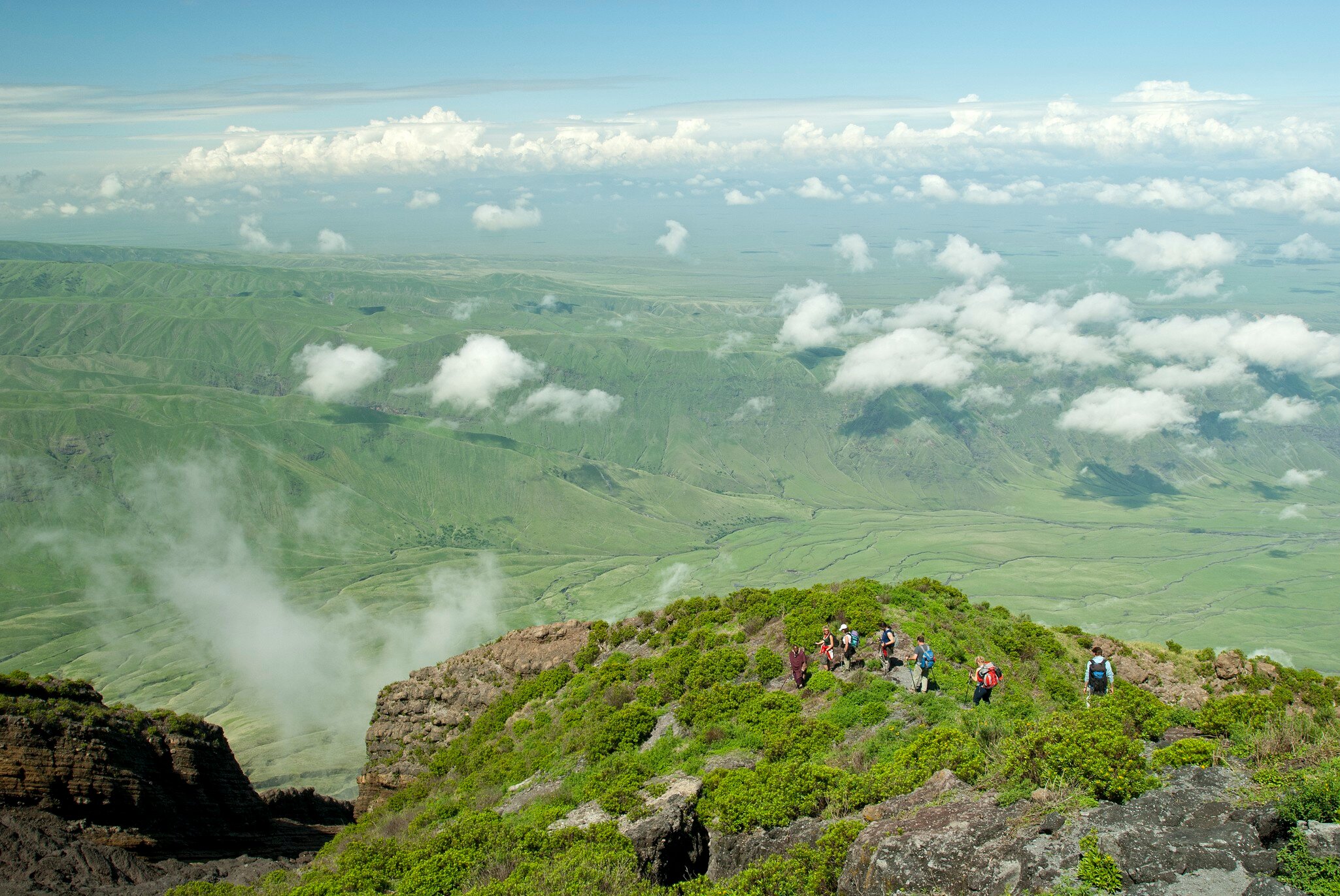 Ol Doinyo Lengai, Tanzania - January 1, 2007: A group of tourists is hiking down from the  top of Ol Doinyo Lengai into the green Rift Valley, in the background the Escarpment of the Rift Valley is visible. In the foreground there is some volcanic...