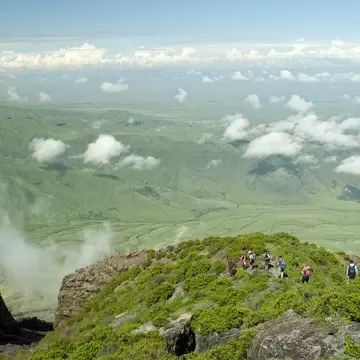 Ol Doinyo Lengai, Tanzania - January 1, 2007: A group of tourists is hiking down from the  top of Ol Doinyo Lengai into the green Rift Valley, in the background the Escarpment of the Rift Valley is visible. In the foreground there is some volcanic...