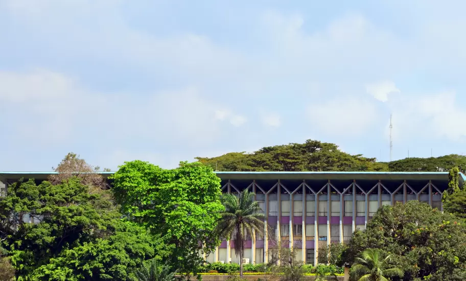 Modernist building with V-shaped concrete columns rising behind tropical trees and palms in Abidjan, Côte d'Ivoire