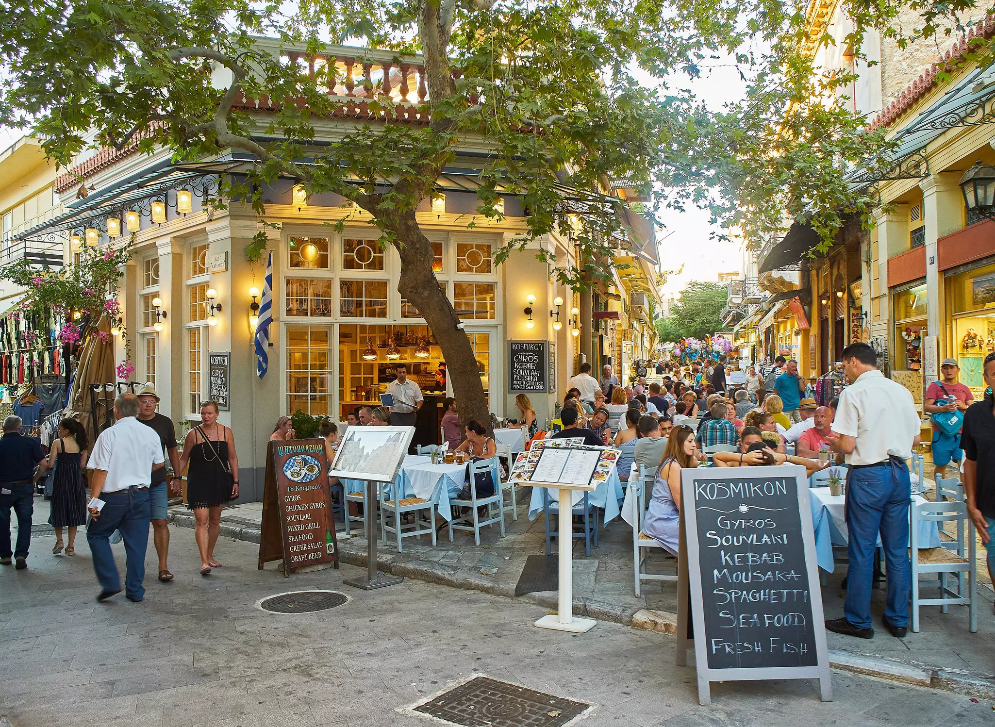 People dining at a terrace of a Greek restaurant in a busy city neighborhood