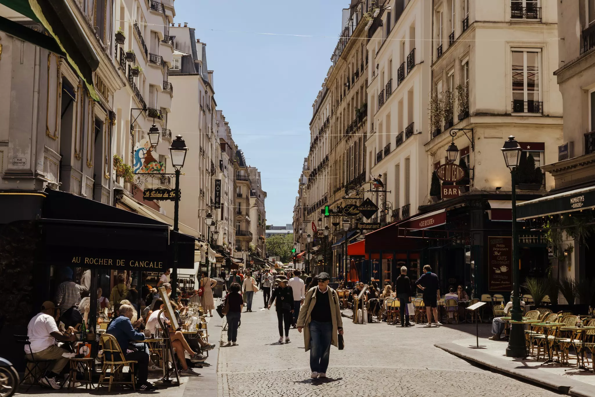 People walking on a cobblestoned street lined with cafes and shops.