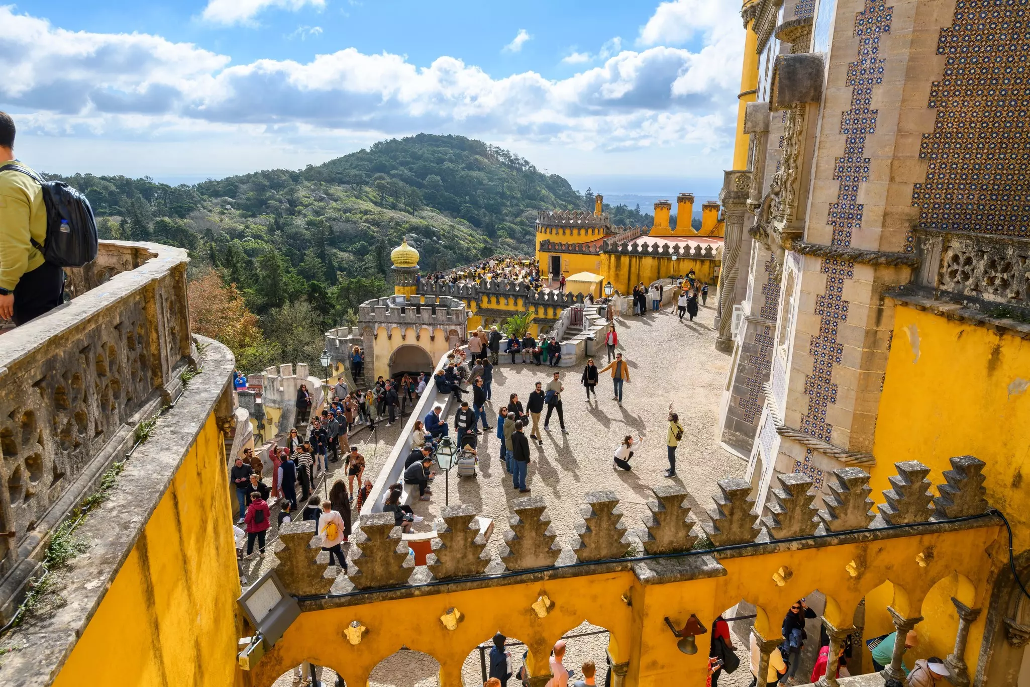 Interior courtyard of a palace with a yellow crenellated walls and lots of tourists