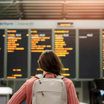 Woman standing in front of a flight departure board at an airport. PeopleImages/Shutterstock