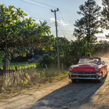 A person driving a vintage car on an unmade road in Viñales, a beautiful and lush valley in Pinar del Río Province, Cuba