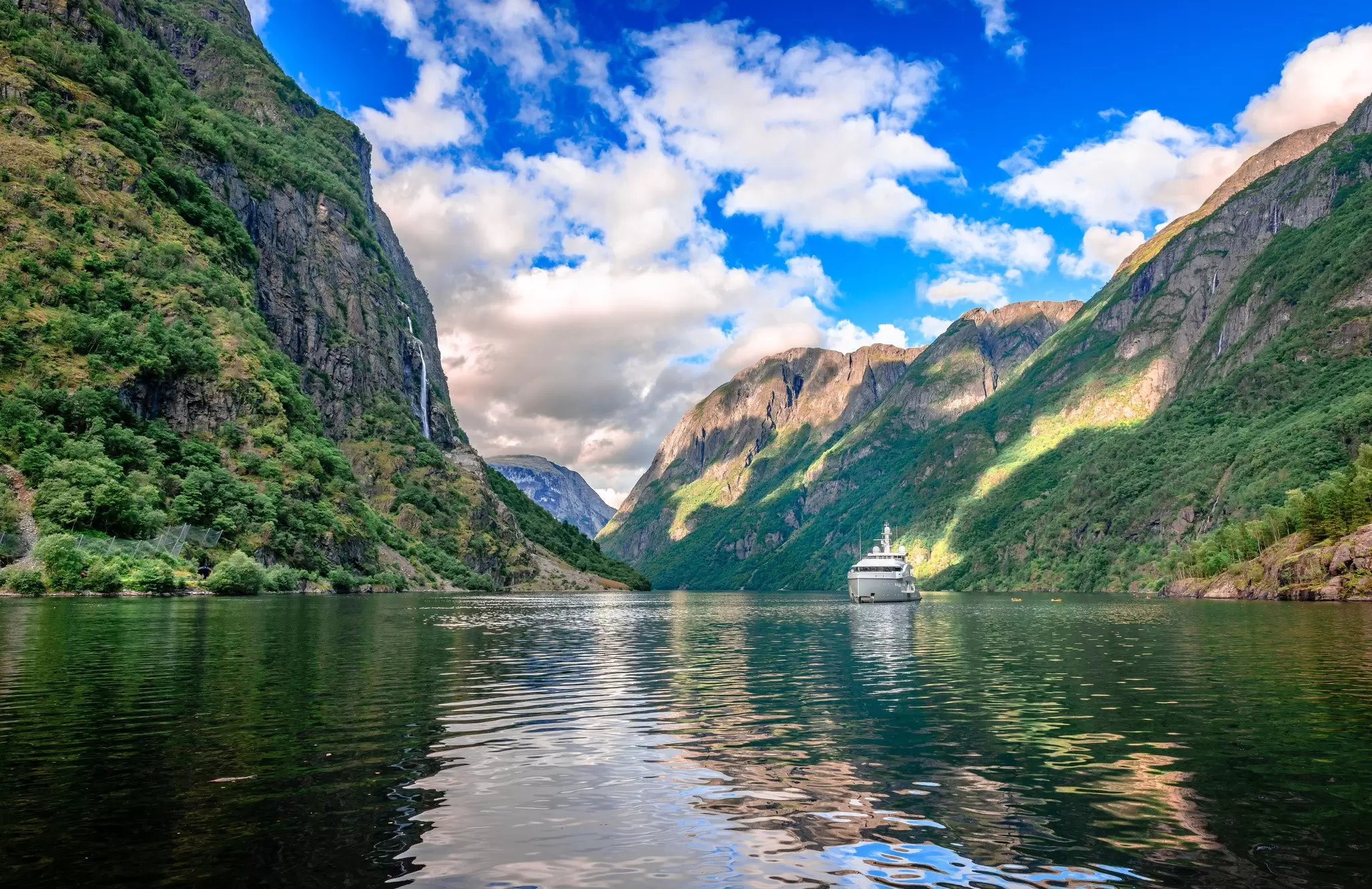 A boat cruises through Aurlandsfjord near Flåm, Norway, with soaring mountains on either side.