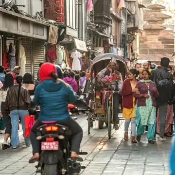 Shoppers, a motorbike and a flower-laden cycle rickshaw crowd the narrow market lane of Asan Tole, Kathmandu.