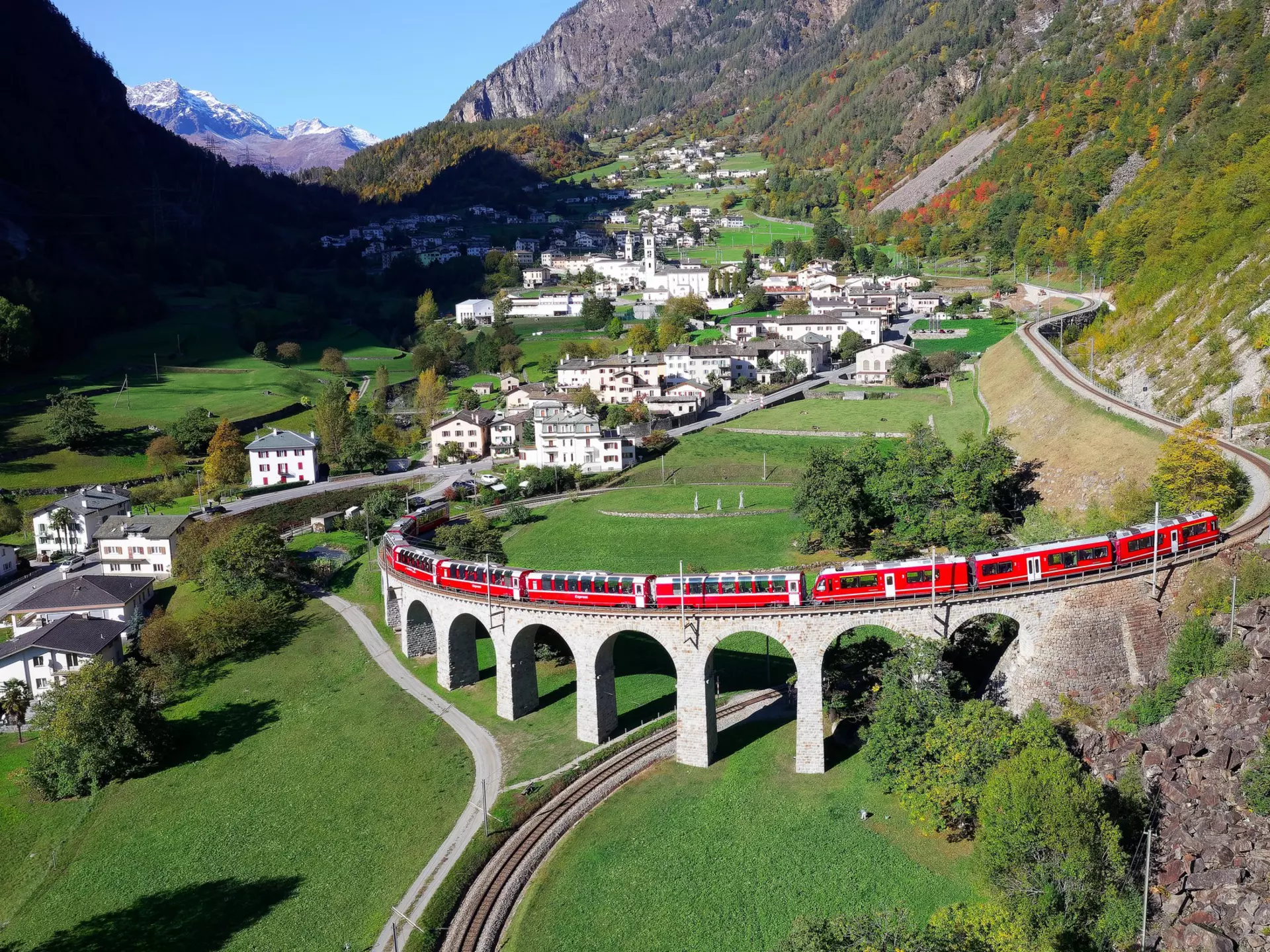 A red train on a raised spiral track over a grassy meadow in Graubünden, Switzerland