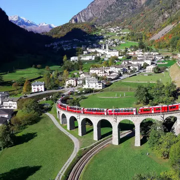 A red train on a raised spiral track over a grassy meadow in Graubünden, Switzerland