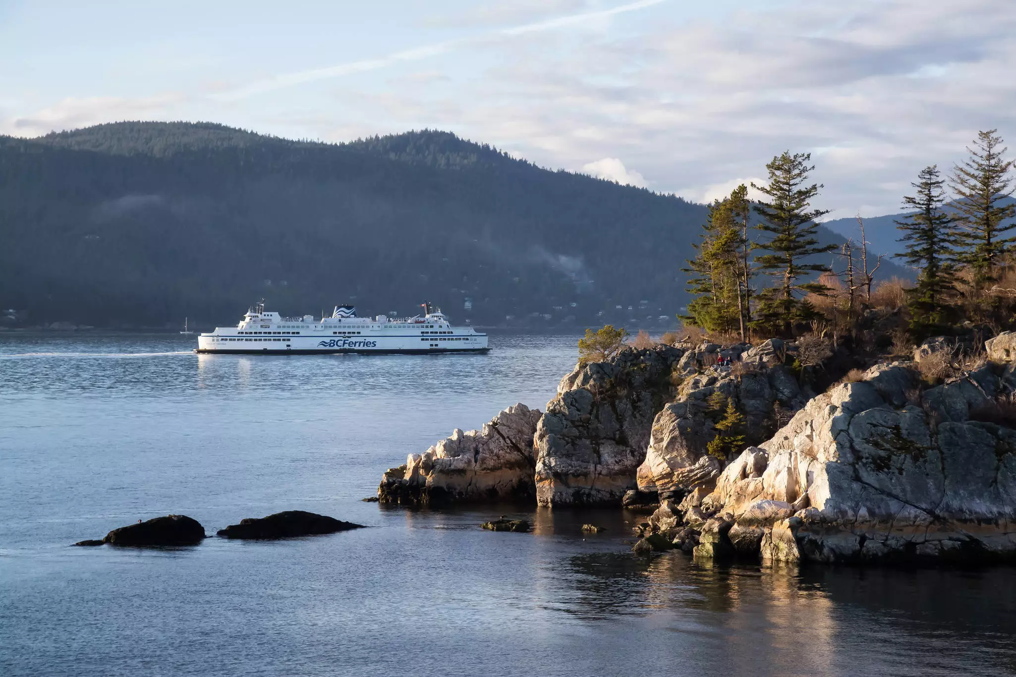 A large white ferry branded "BCFerries" passes between forest-covered islands.