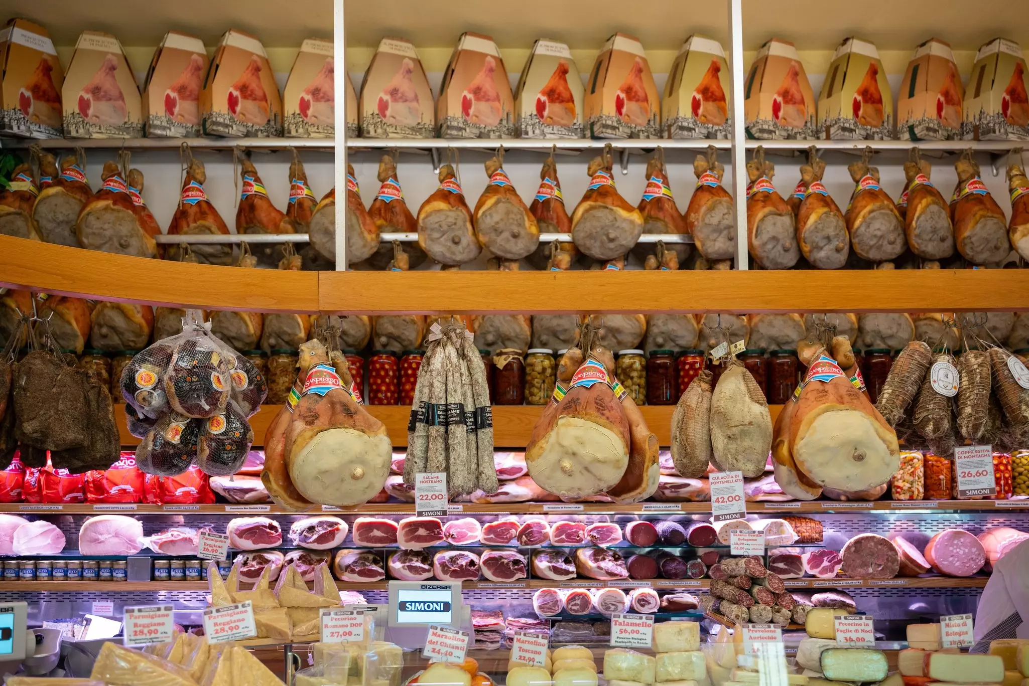 Prosciutto and salami hanging behind a cheese counter in a shop.