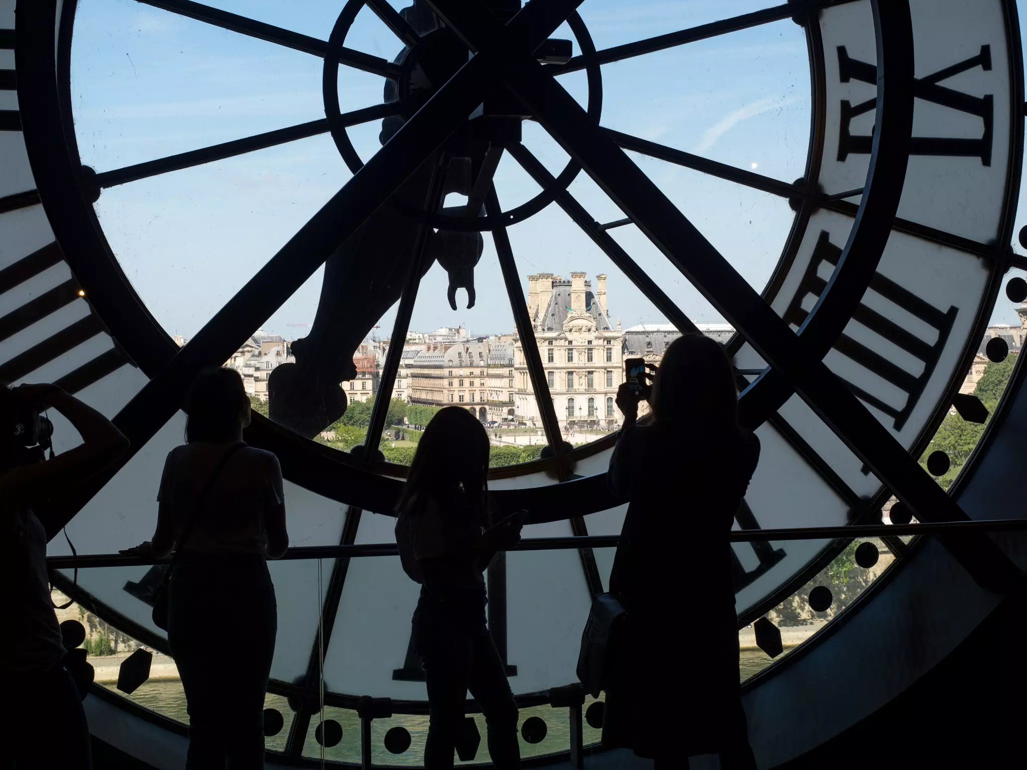 People in silhouette stand in front of a glass clock face with light shining through it.