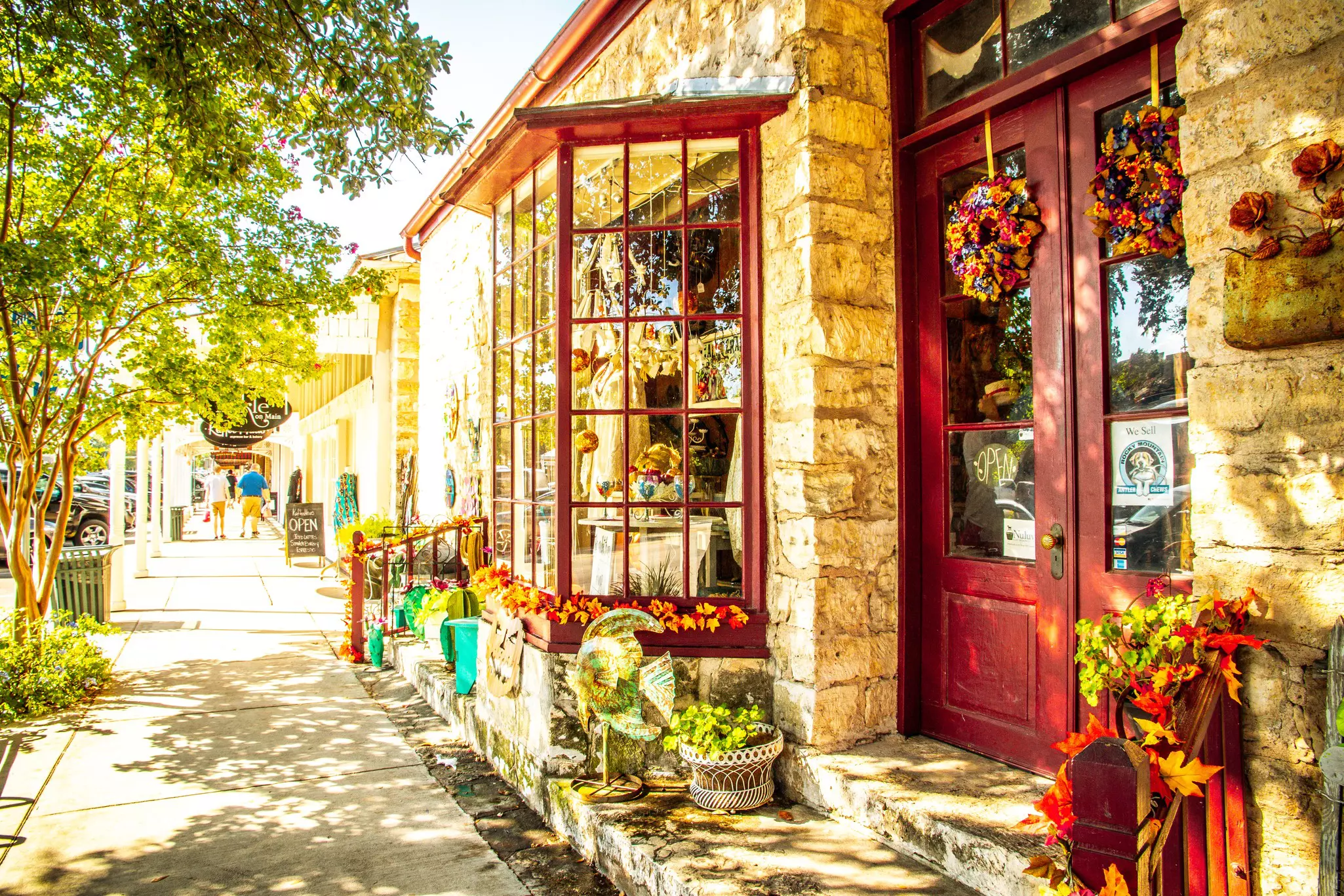 A storefront with stone columns and red-painted door and windows along a street in a small town.