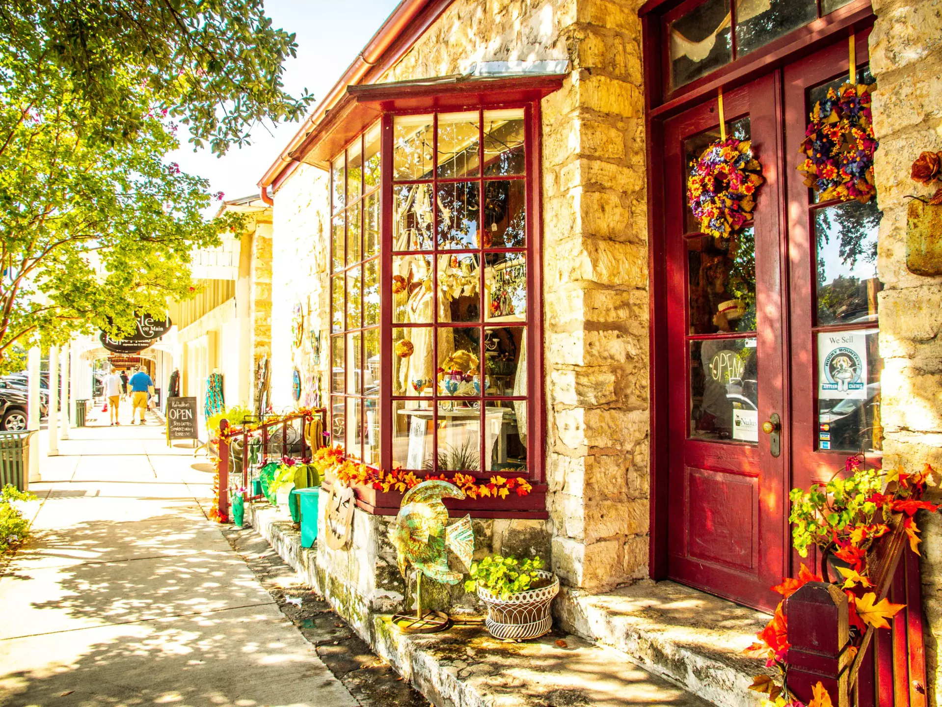 A storefront with stone columns and red-painted door and windows along a street in a small town.