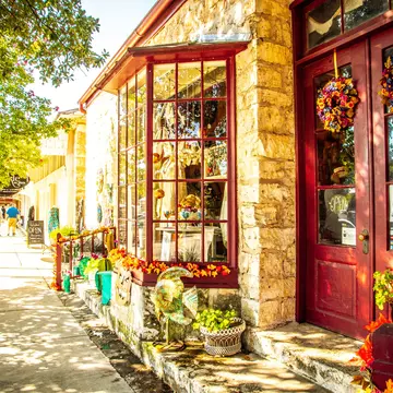 A storefront with stone columns and red-painted door and windows along a street in a small town.