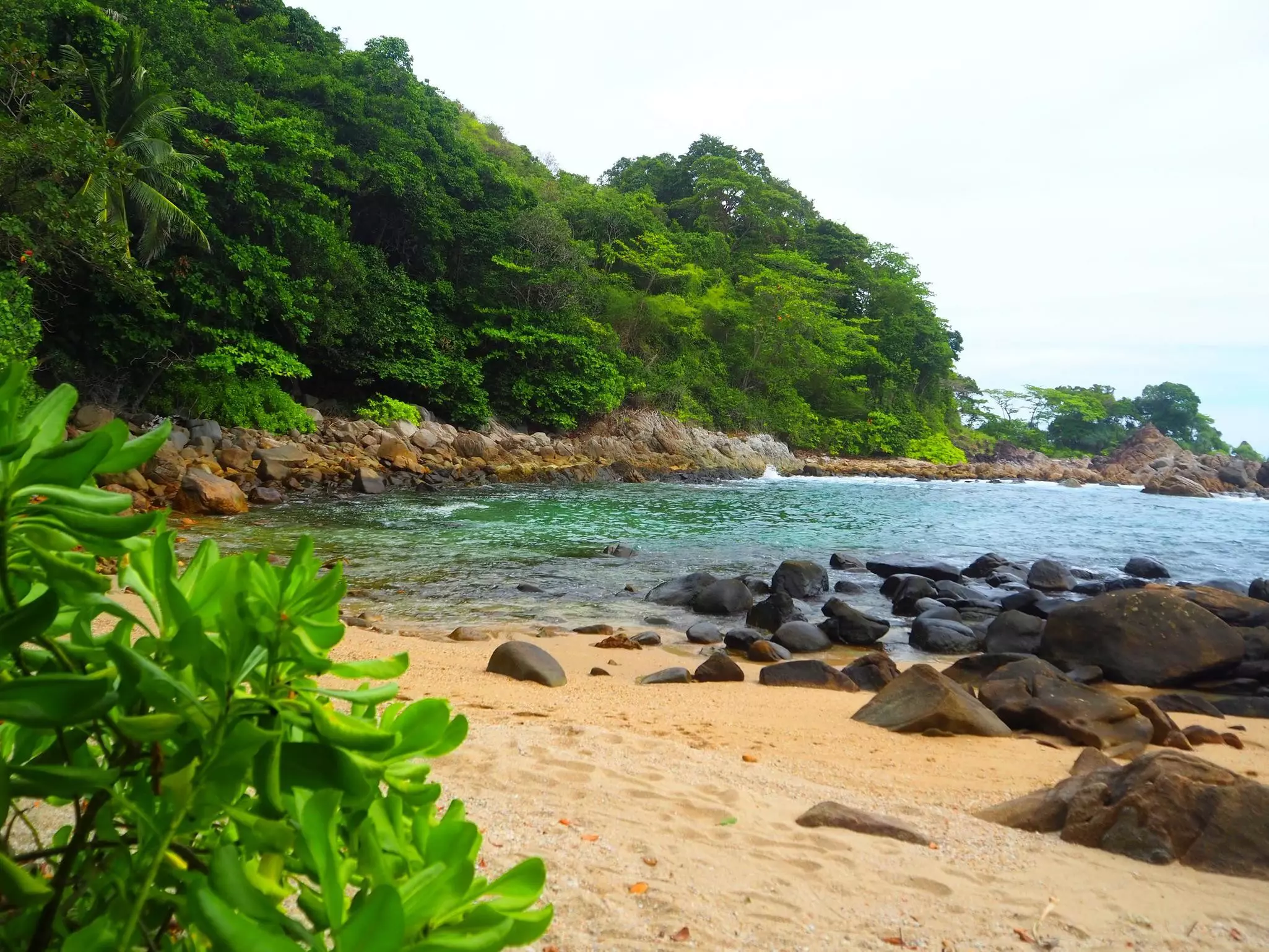 A golden-sand cove with large boulders creating a sheltered shoreline.