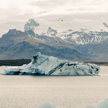 Blue icebergs in a lagoon under cloudy skies, with a snow-covered glacier on the far shore.