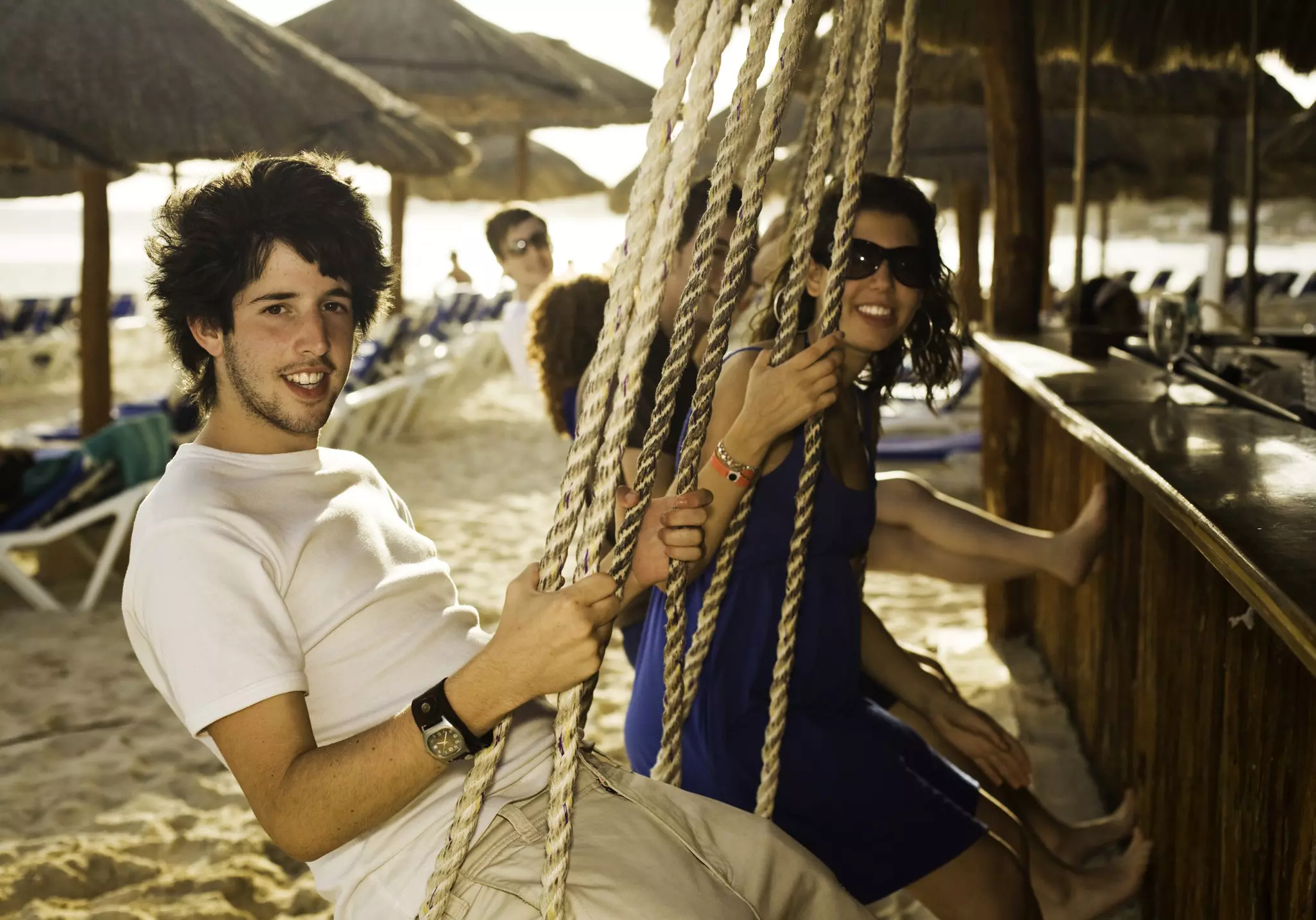 Teenagers on rope-swings at the beach